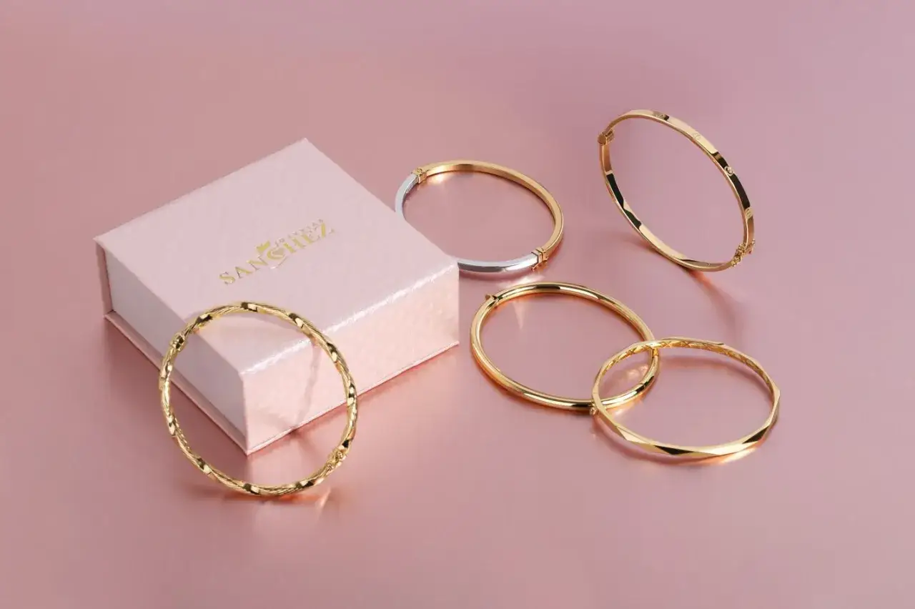 Elegantes brazaletes dorados y uno bicolor, junto a una caja de joyer&iacute;a. Los nombres de joyas como estos brillan con estilo.