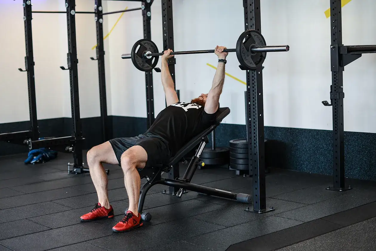 Mężczyzna wykonuje wyciskanie na ławce skośnej z sztangą. Ćwiczy klatkę piersiową w siłowni.