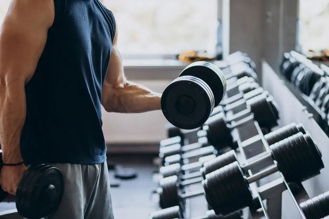 Ein Bodybuilder hebt eine Hantel im Fitnessstudio. Muskeln sind sichtbar, während er trainiert.