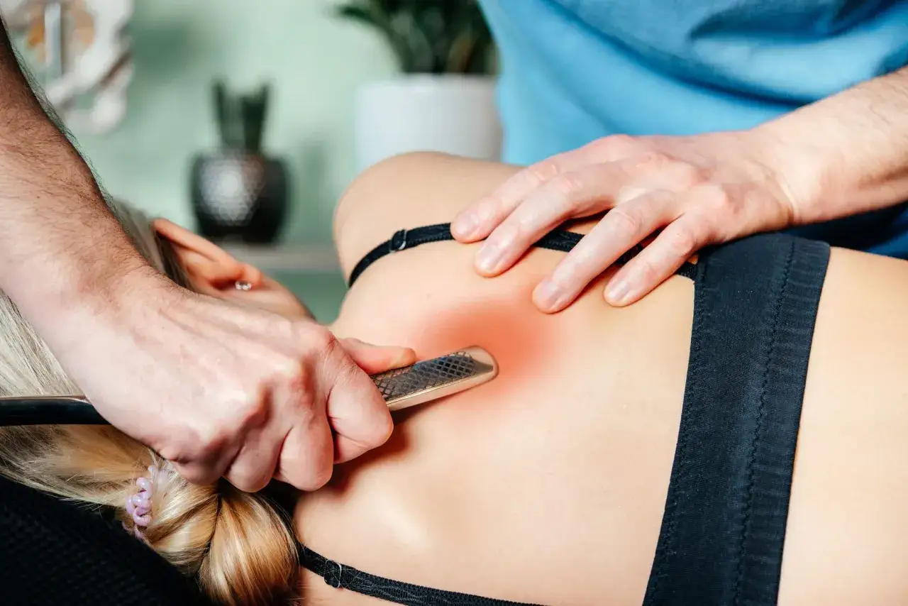Th&eacute;rapeute utilisant un outil pour soulager une grosse contracture musculaire dans le dos d'une femme.