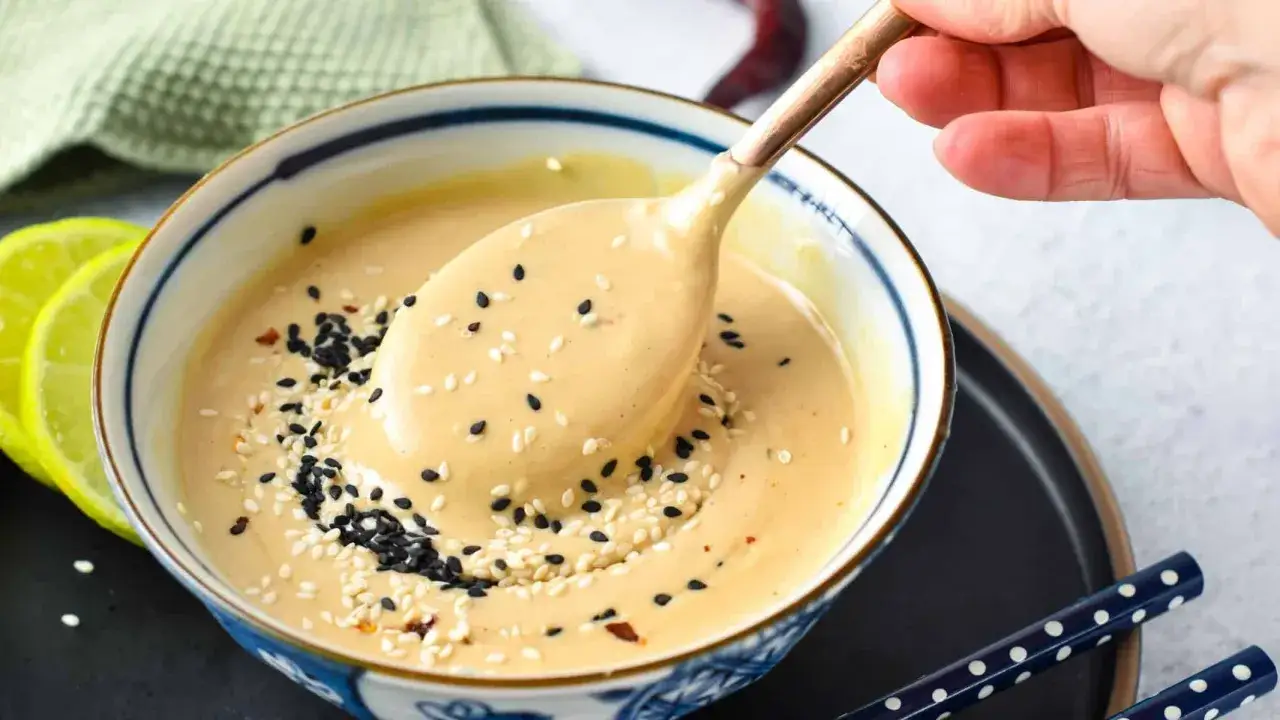 A creamy tahini dressing, sprinkled with black and white sesame seeds, is scooped from a bowl. This savory miso vs tahini debate is settled with this delicious sauce.