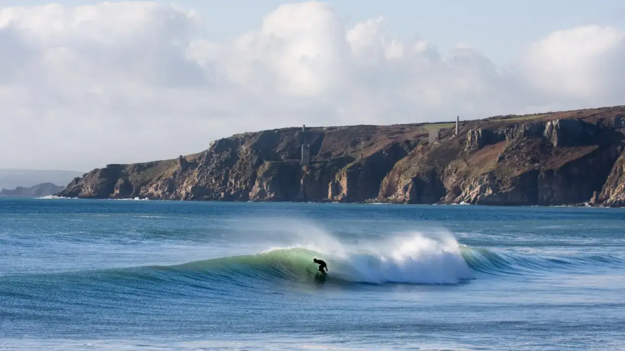 Ein Surfer reitet eine gr&uuml;ne Welle vor der dramatischen K&uuml;ste Cornwalls.