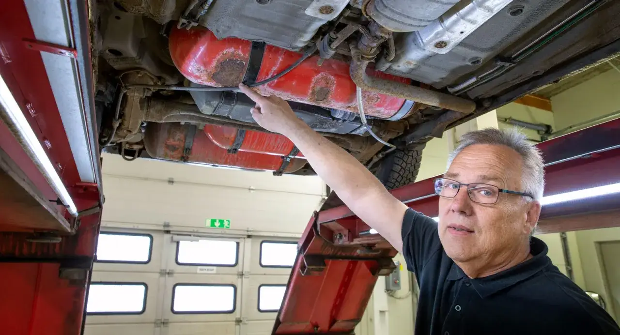 Mekaniker pekar på en rostig tank under en lpg bil.