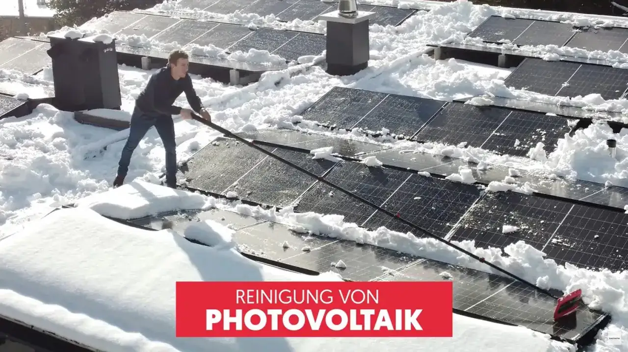 Młody mężczyzna odśnieża panele fotowoltaiczne na dachu. Śnieg zalega na panelach, utrudniając ich pracę.