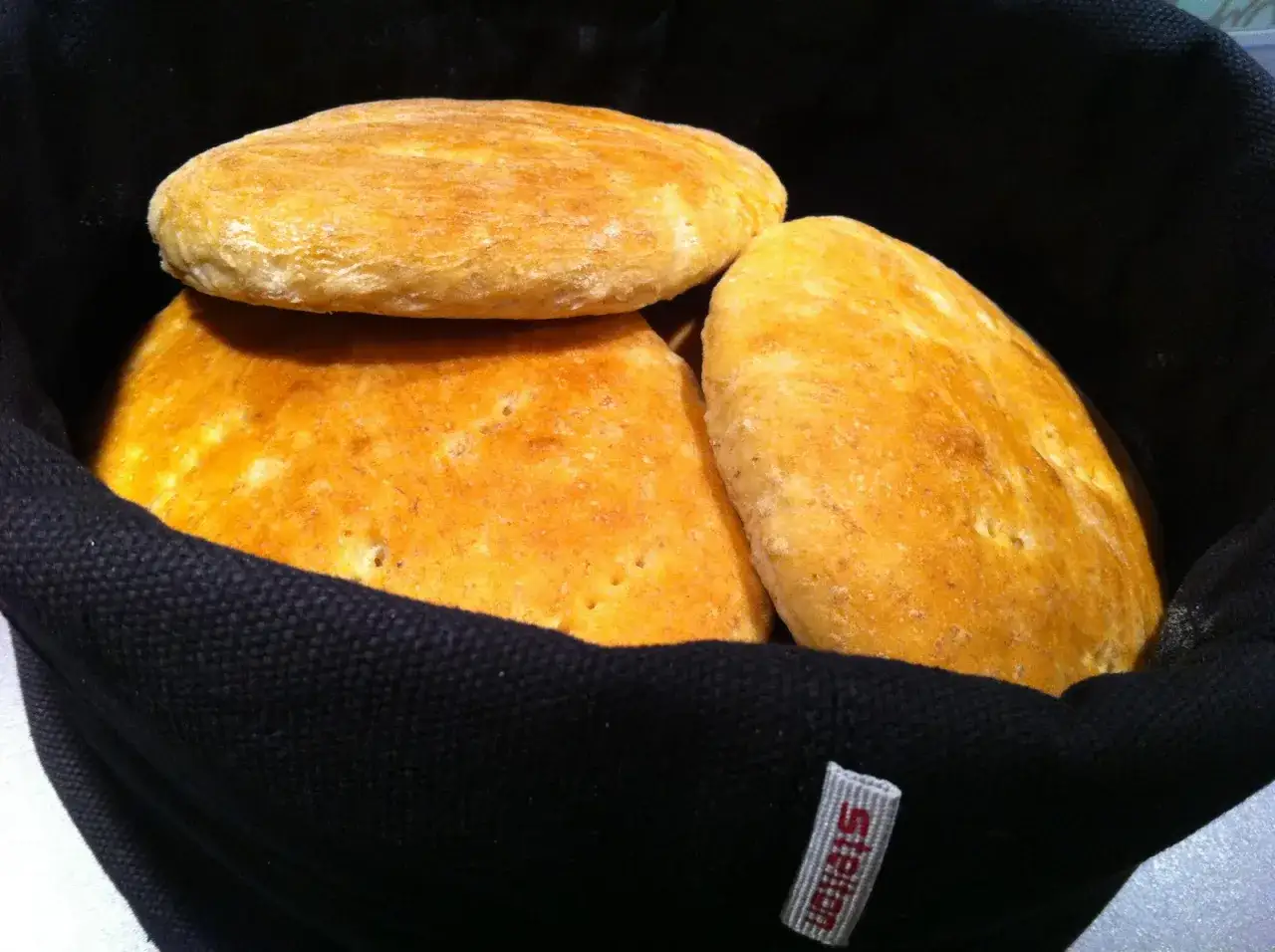 Tre gyllene tekakor med havregryn ligger i en svart korg. Perfekta för frukost eller fika.