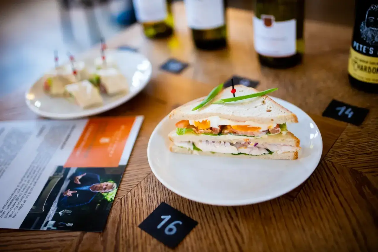 Pyszny sandwich z kurczakiem i jajkiem, obok menu Mielżyński i butelki wina.