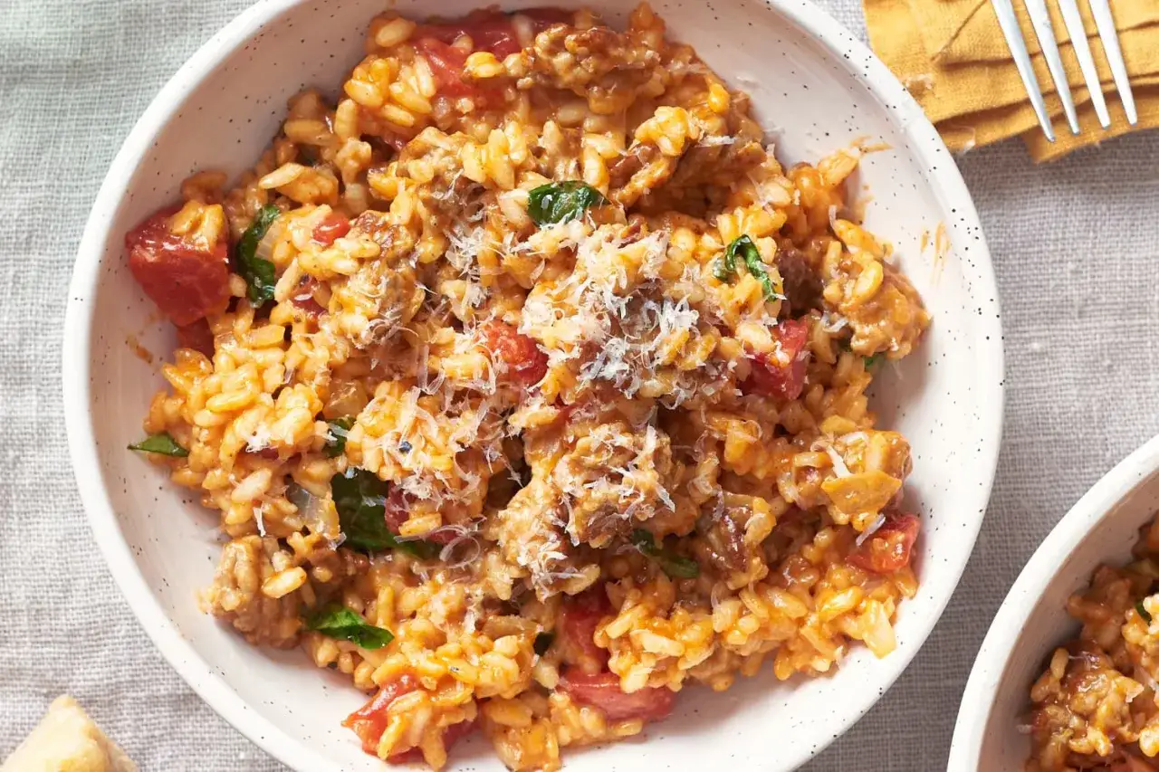 Un cremoso risotto salsiccia con trozos de tomate y espinacas, espolvoreado con queso rallado.