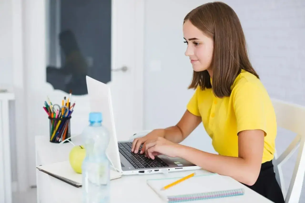 Dziewczyna w żółtej koszulce uczy się programowania na laptopie. To jej pierwszy krok do pracy dla informatyka bez doświadczenia.