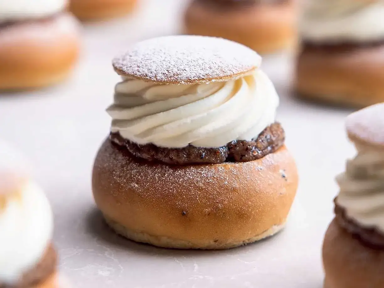 En närbild av en nyttig semla med fluffig grädde och mandelmassa, pudrad med florsocker. Flera semlor i bakgrunden.