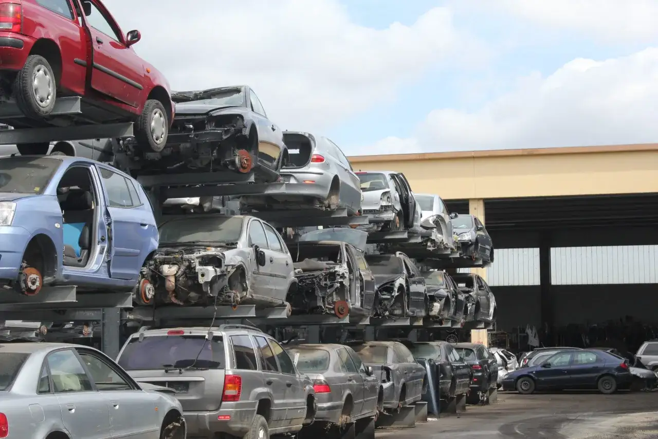 Rottamazione auto: un deposito di veicoli accatastati, alcuni senza ruote o parti, in attesa di smaltimento.