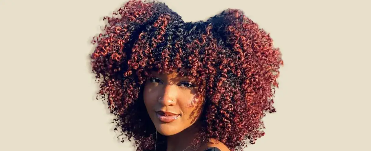 Mujer con cabello rizado y oscuro con mechas rojizas, peinado en dos moños altos.