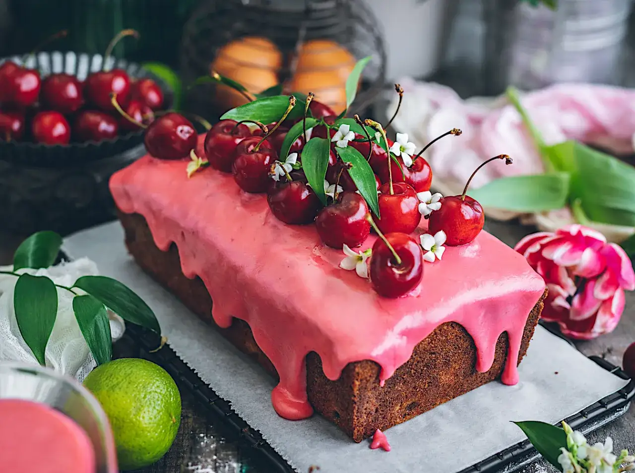 Bizcocho de cerezas cubierto con glaseado rosa y decorado con cerezas frescas y hojas verdes.