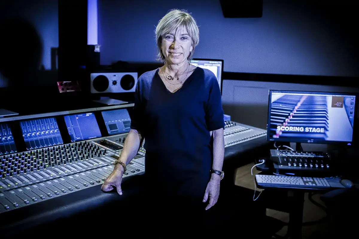 Mujer sonriente en estudio de grabación, rodeada de consolas y monitores. Ella sabe como ser manager de éxito en la industria musical.