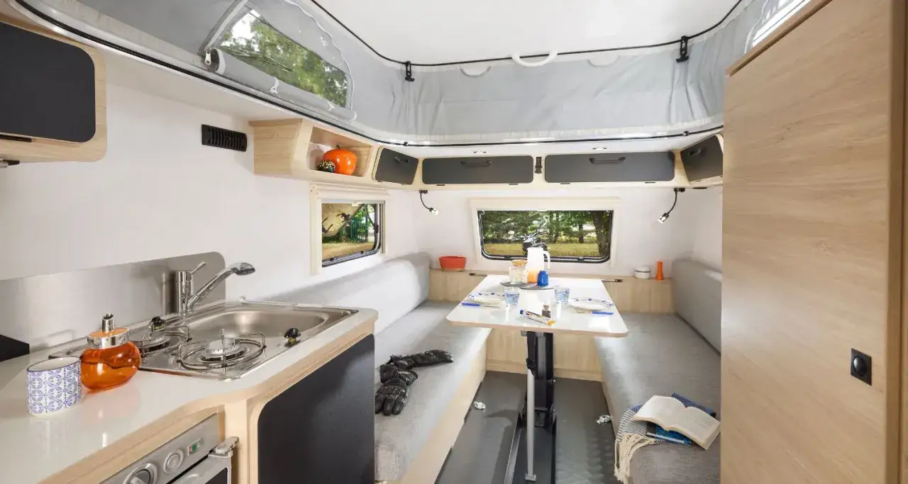 Int&eacute;rieur d'une caravane simple avec coin repas, cuisine et banquettes. Un espace fonctionnel pour voyager.