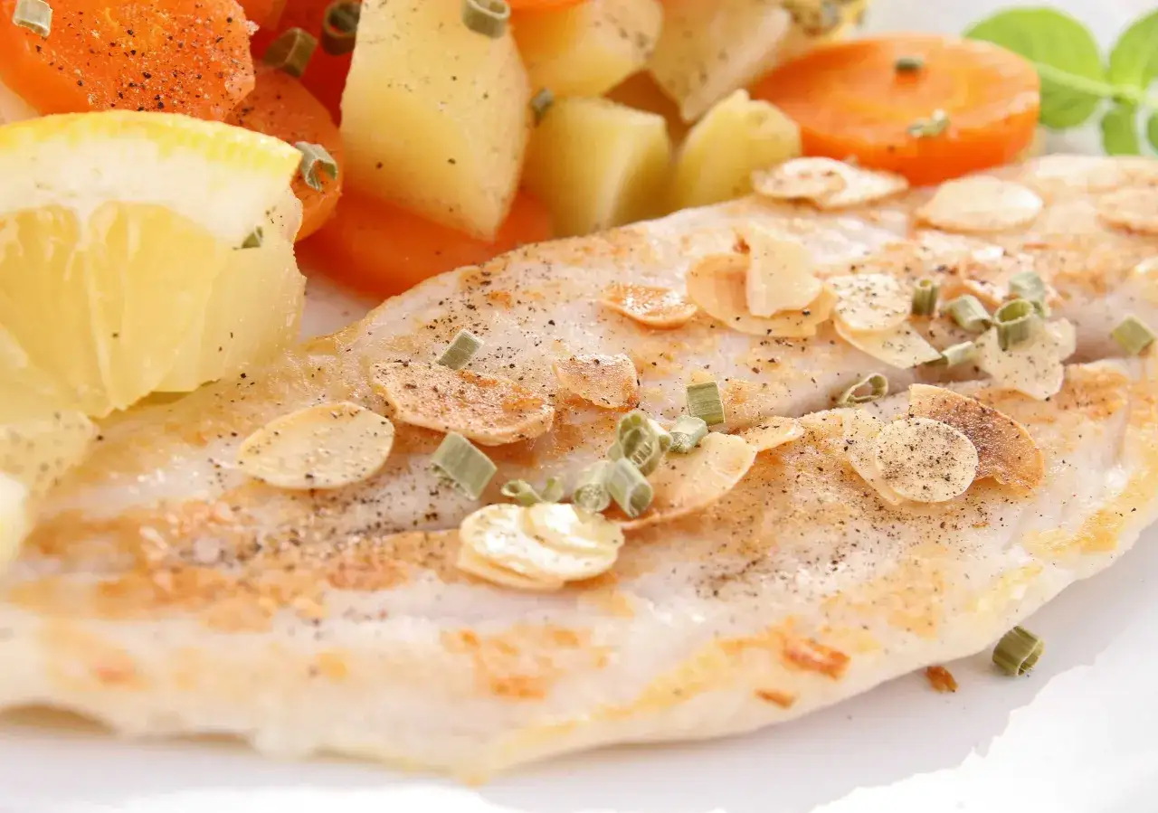 Delicioso lenguado beb&eacute; a la plancha, adornado con l&aacute;minas de almendra y cebollino, acompa&ntilde;ado de zanahorias y patatas.