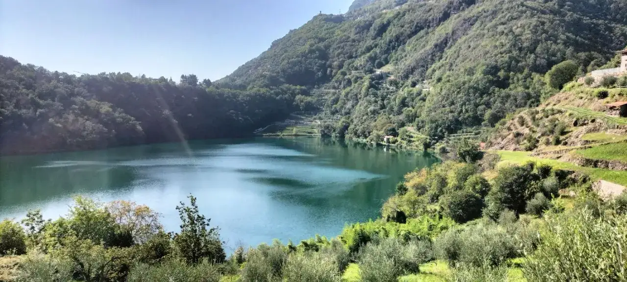 Lago alpino con acque verdi, circondato da colline boscose e terrazzamenti coltivati. Un angolo terme naturale e rigenerante.