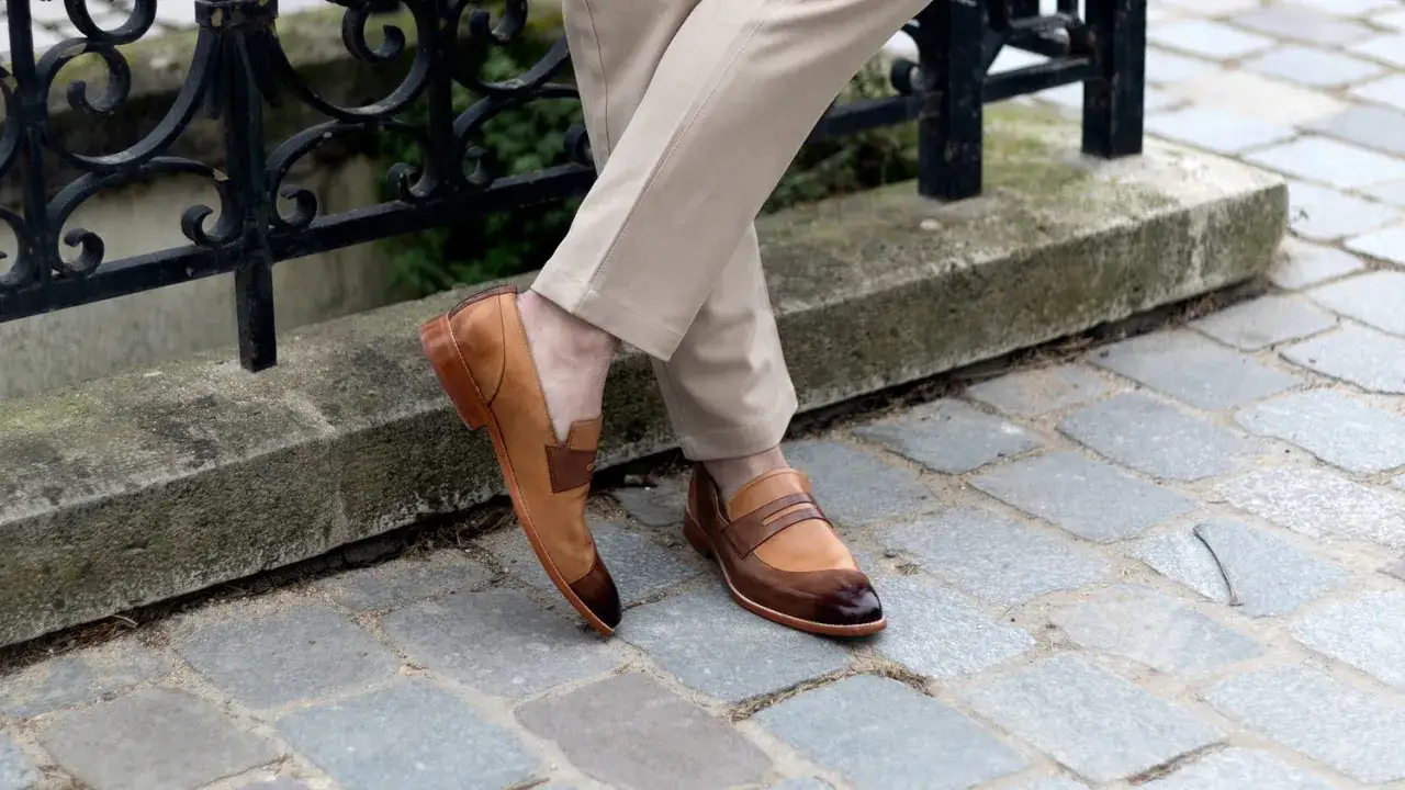 Un homme porte une tenue élégante avec une chaussure marron homme, un pantalon beige et est assis près d'une rambarde.