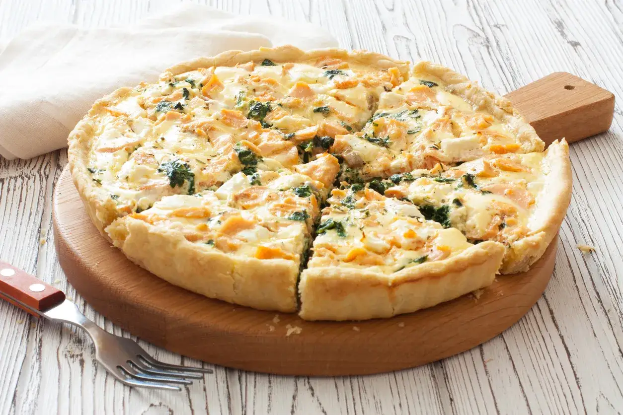 Pyszna tarta z łososiem, szpinakiem i serem feta, pokrojona na kawałki, czeka na talerzu.