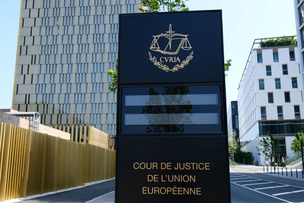 Tablica informacyjna przed budynkiem Trybunału Sprawiedliwości Unii Europejskiej (TSUE). W tle nowoczesne budynki.