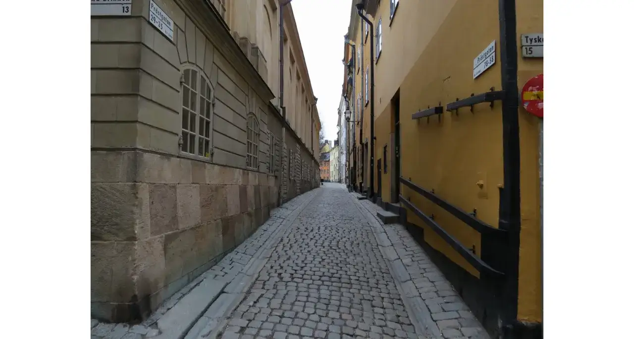 En kullerstensbelagd gränd i **altstadt stockholm** med höga, färggranna hus på båda sidor.