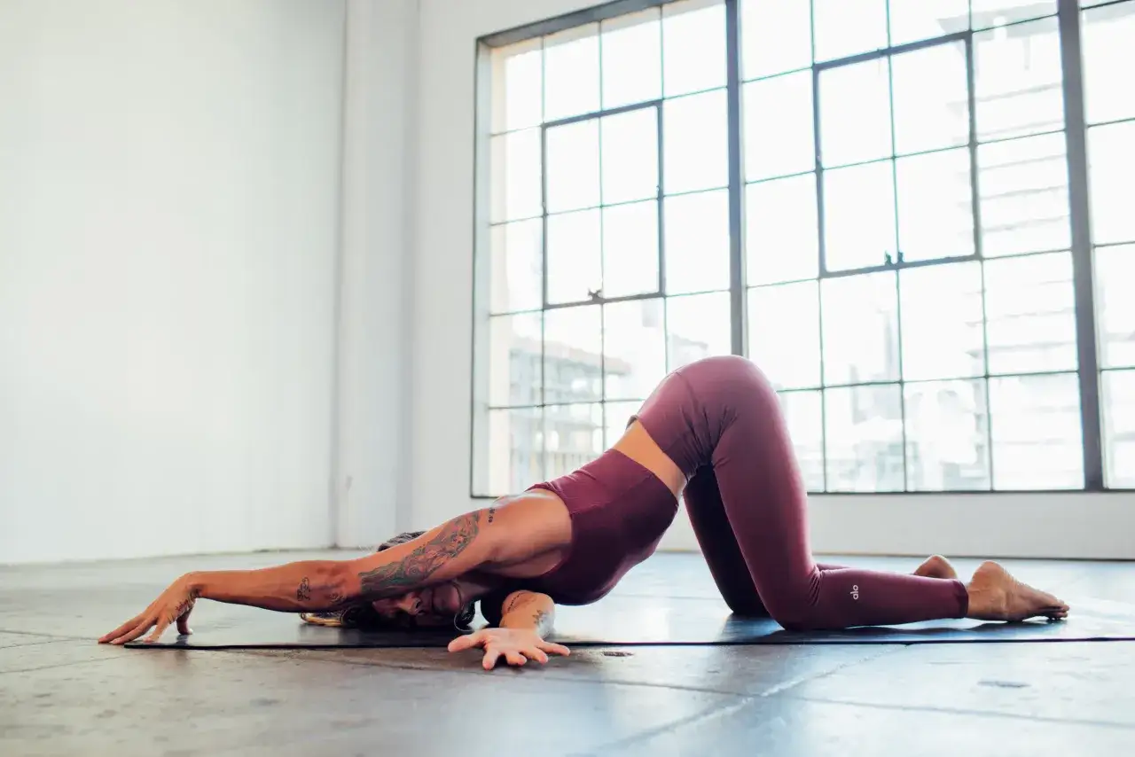 Donna in posa yoga, con un braccio esteso e la testa appoggiata a terra, in una variante di Adho Mukha Svanasana.