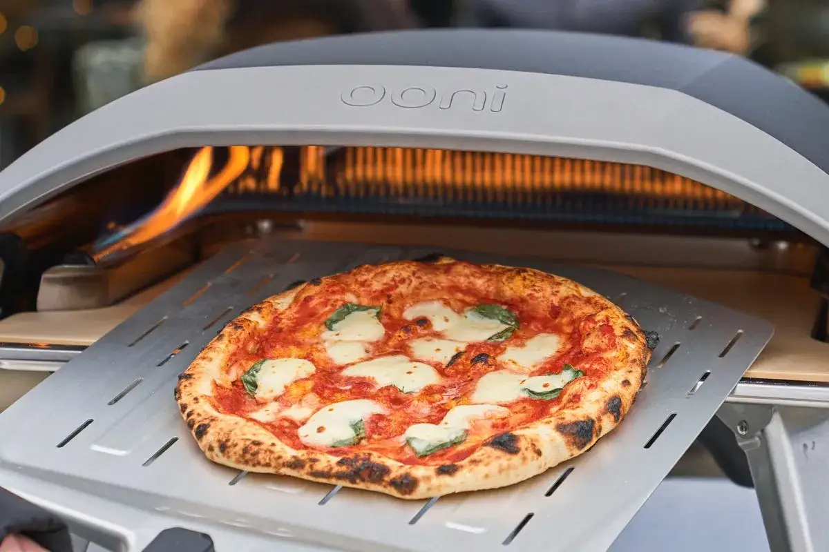 En perfekt Margherita-pizza tas ur en Ooni pizzaugn. Den gyllene ooni pizzadegen har bubblor och lite br&auml;nda kanter.