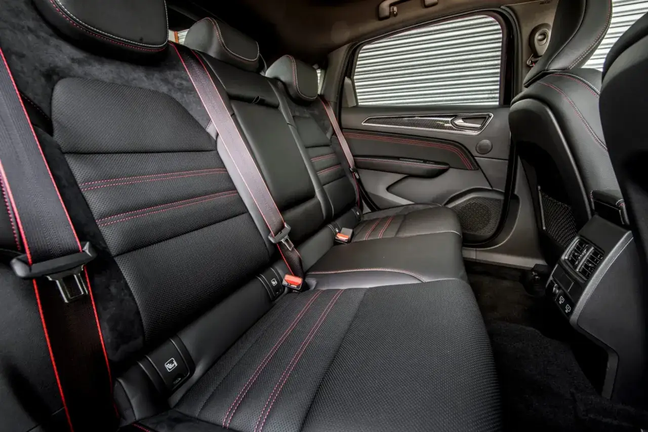 Intérieur du Renault Arkana : sièges arrière en cuir noir avec surpiqûres rouges, ceintures de sécurité rouges. Confort et style.