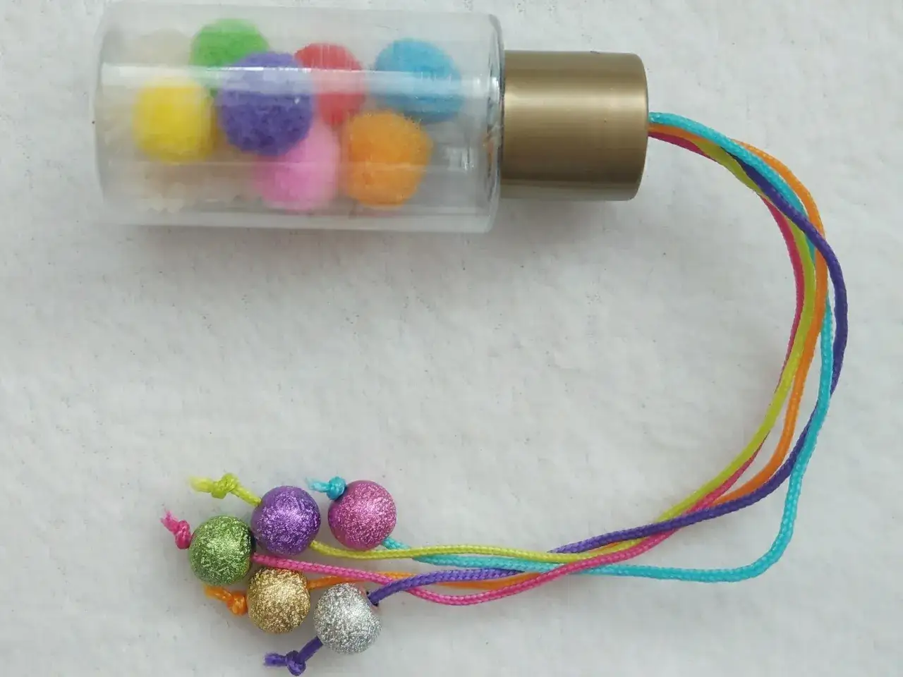 Buntes Rassel-Spielzeug zum selber machen für 1 Jahr: Pompons in einer Flasche, bunte Schnüre mit Glitzerkugeln.