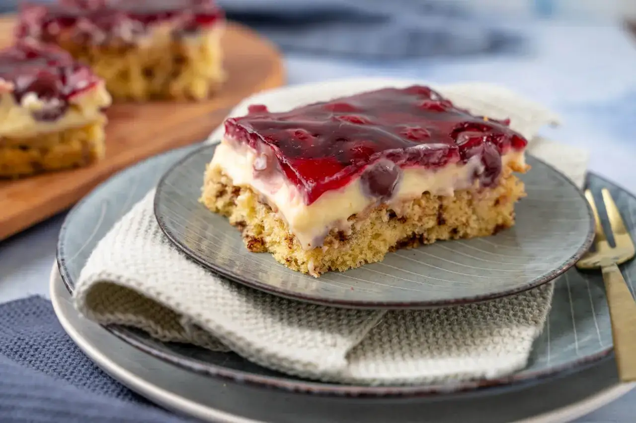 Ein St&uuml;ck Kirschtorte mit Pudding und Kirschgelee. Der saftige Boden ist mit einer cremigen Puddingschicht und vielen Kirschen belegt.