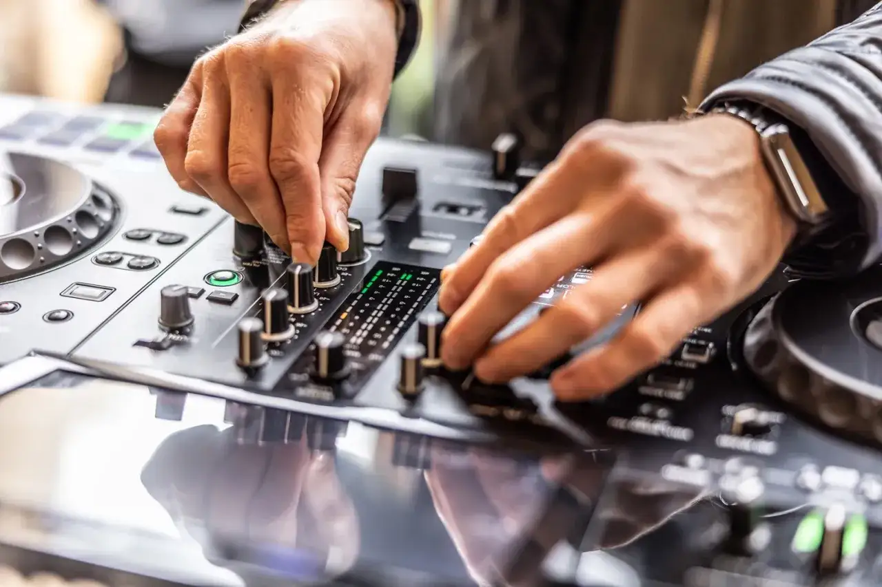 Ręce DJ-a miksujące muzykę na konsoli. Chcesz wiedzieć, jak zostać DJ-em? To właśnie od tego zaczynają się pierwsze kroki.