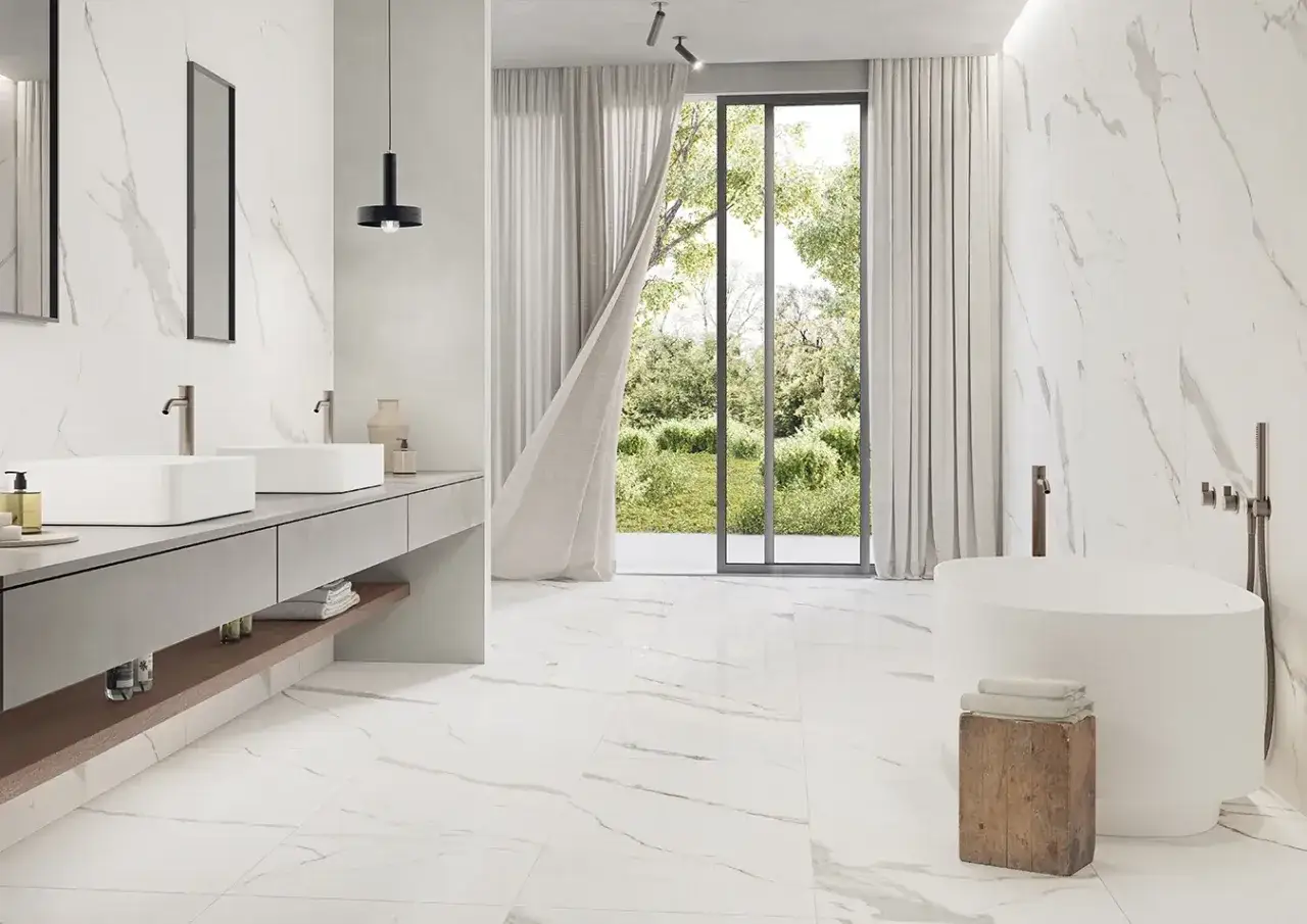 A modern bathroom with white marble tile and light grey grout, featuring a freestanding tub and double vanity.