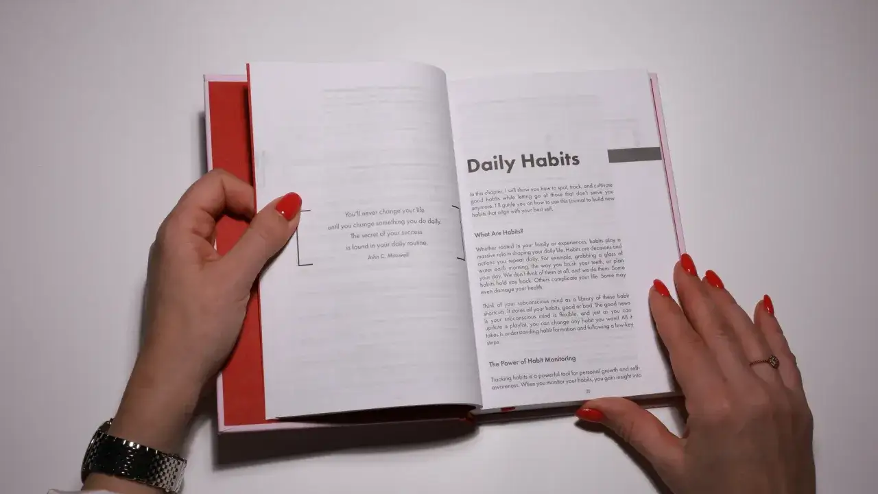 A hand with red nails turns a page in a book titled