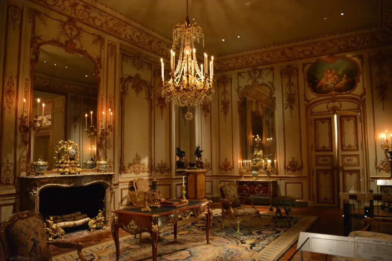 A lavish room with a crystal chandelier, ornate gold trim, and antique furniture embodies the royalcore aesthetic.