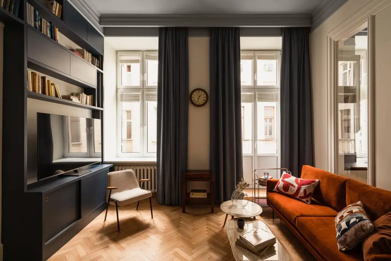 Eklektyczny salon z pomarańczową kanapą, regałem z książkami i telewizorem, jasnym fotelem i marmurowymi stolikami.