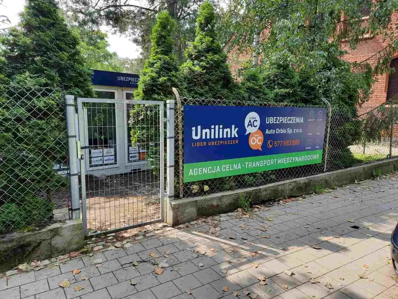 Baner reklamowy z logo Unilink i informacją o ubezpieczeniach przed ogrodzeniem.