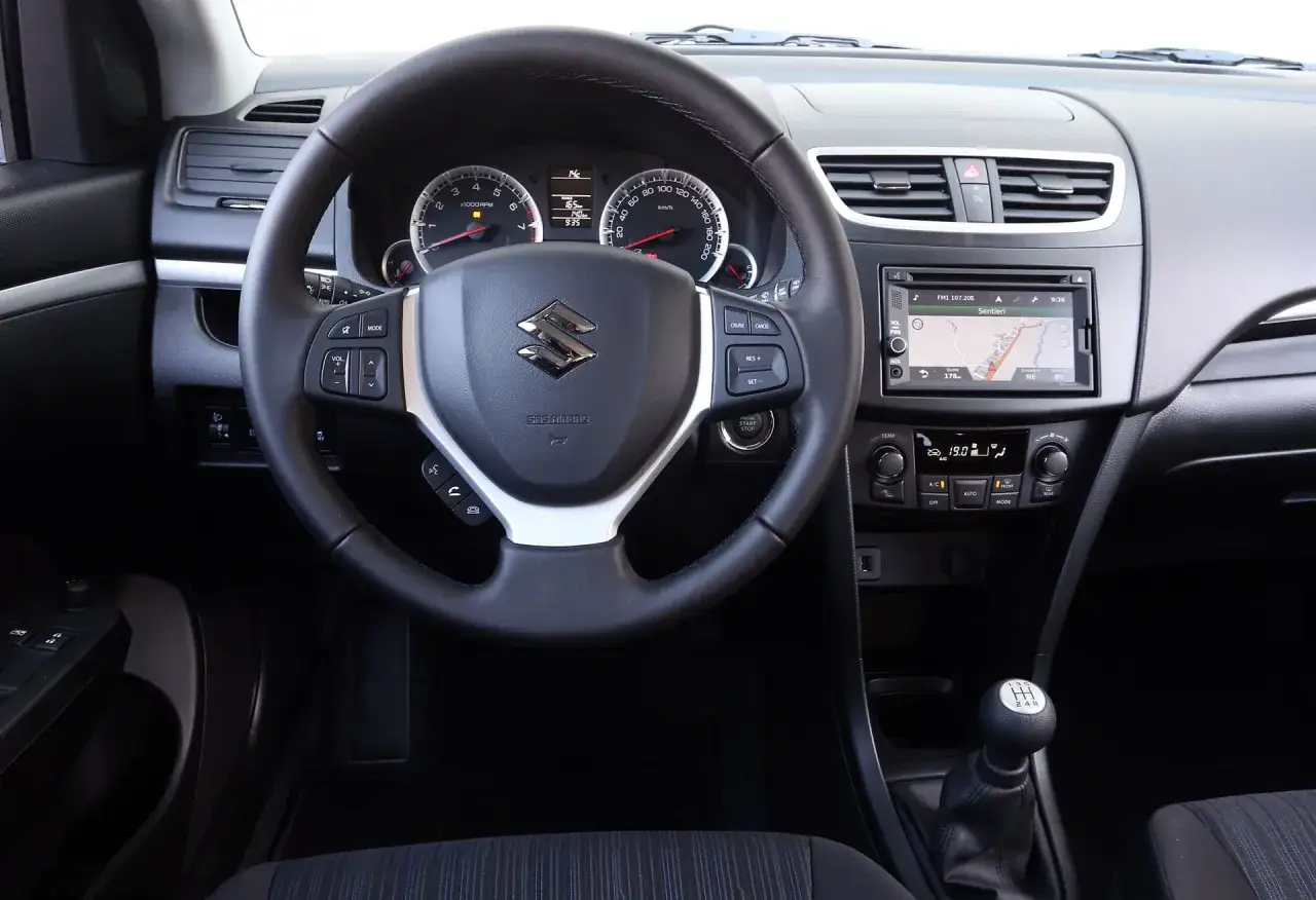 Wnętrze Suzuki Swift, idealne do miasta. Kierownica z przyciskami, nawigacja i manualna skrzynia biegów. Dobre opinie o tym modelu.