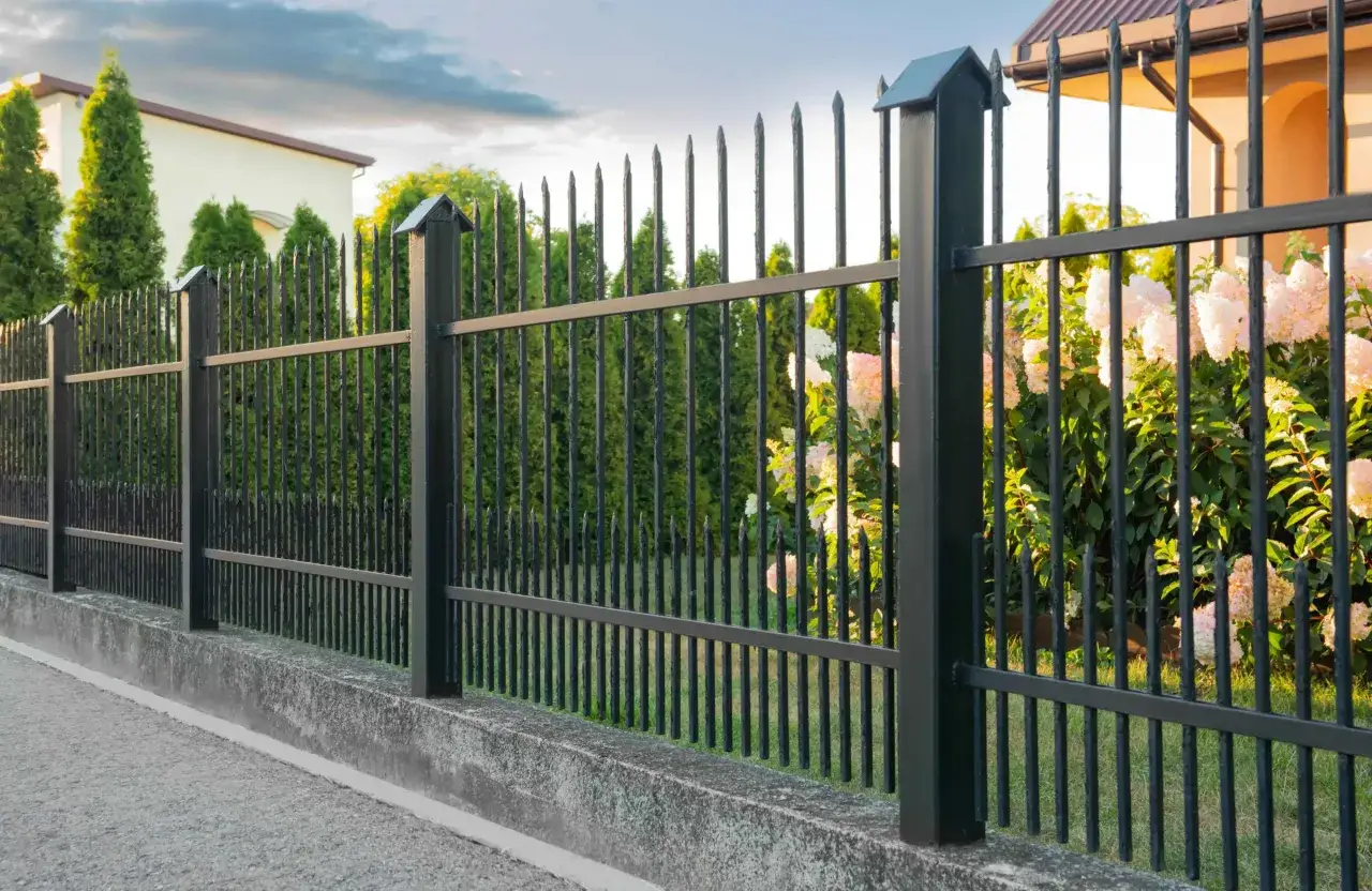 Czarna, metalowa podmurówka ogrodzenia z betonu, otoczona zielenią i kwiatami. Idealna do malowania farbą antykorozyjną.