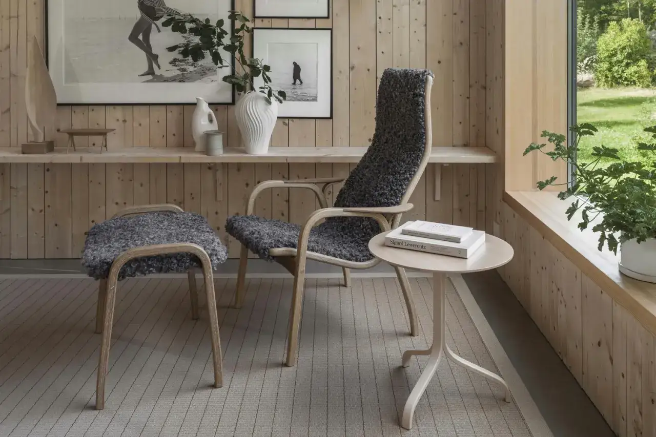 En stol och pall med f&aring;rskinn, i en stil som p&aring;minner om norsk design, st&aring;r i ett rum med tr&auml;v&auml;ggar.
