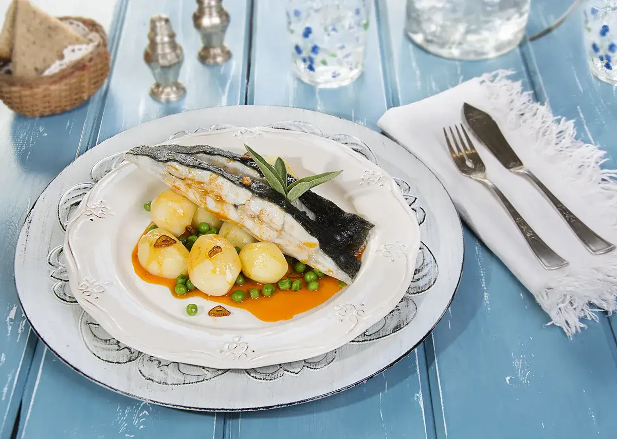 Rodaballo gallego servido con patatas y guisantes en una salsa naranja. Un plato elegante para disfrutar.