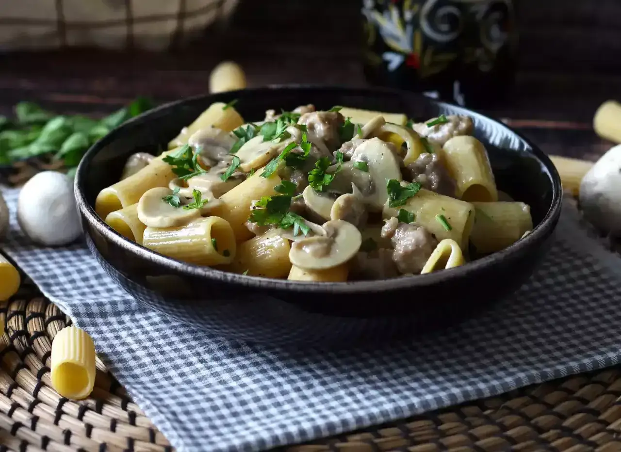 Pasta con burrata y champi&ntilde;ones, cremosa y deliciosa, servida en un cuenco oscuro con perejil fresco.