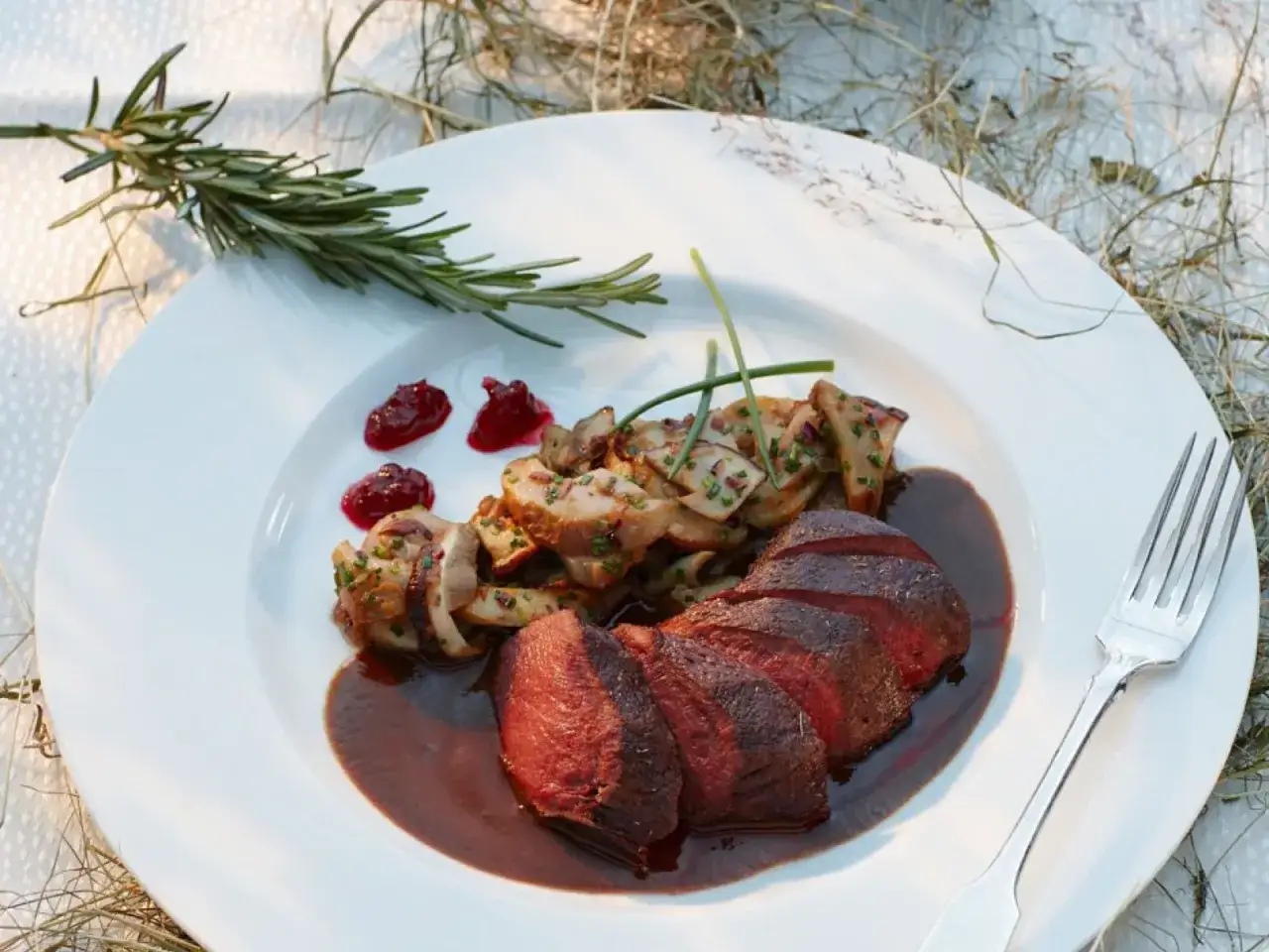 Ein köstliches Rehhals-Rezept: Zartes Rehfleisch mit Pilzen, Preiselbeeren und einer kräftigen Sauce auf einem weißen Teller.