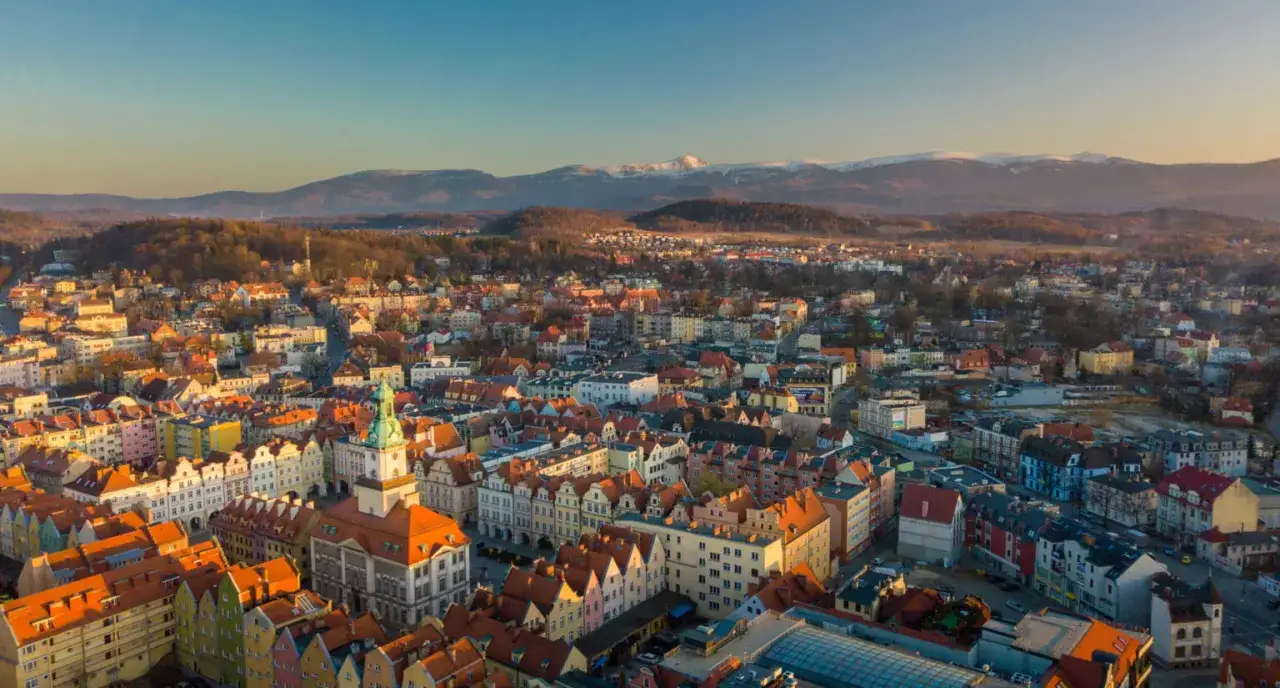 Widok na Jelenia Górę z górami w tle. Kolorowe kamienice i ratusz zachęcają do odkrywania atrakcji miasta.