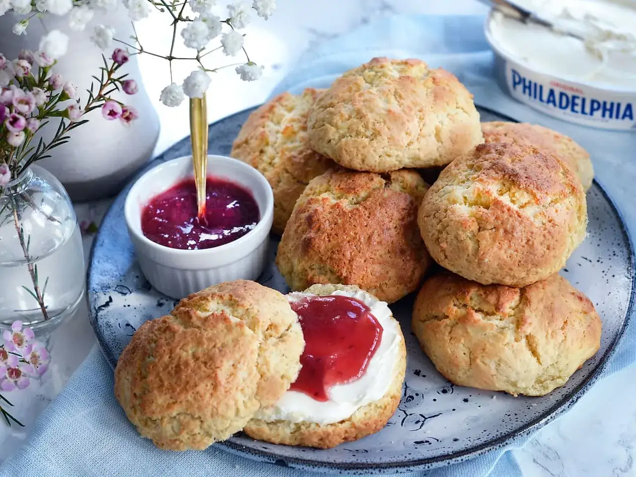 En hög med klassiska scones, en skål med sylt och en burk färskost. En perfekt fika!