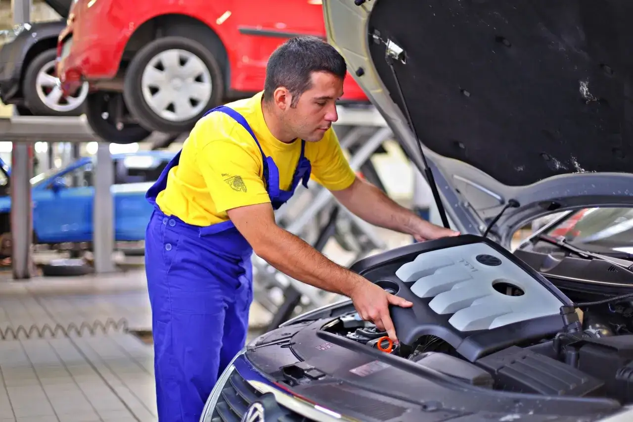 Mechanik w żółtej koszulce i niebieskich ogrodniczkach sprawdza silnik. Zastanawiasz się, ile zarabia mechanik?