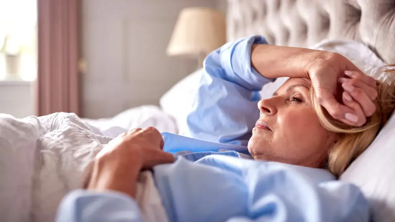 Frau im Bett mit Stirnband, leidet unter Schlafproblemen in den Wechseljahren.