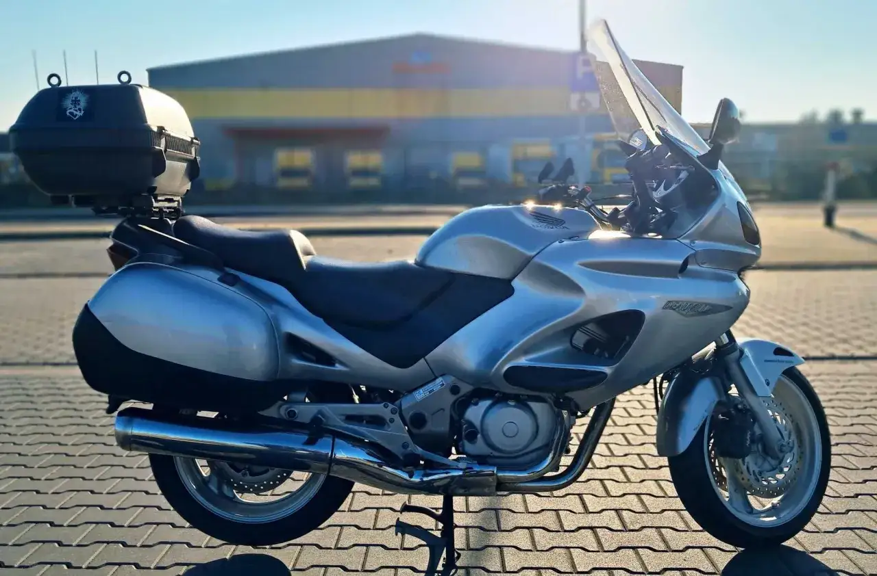 Srebrna Honda Deauville z kufrem i sakwami, gotowa na podróż.