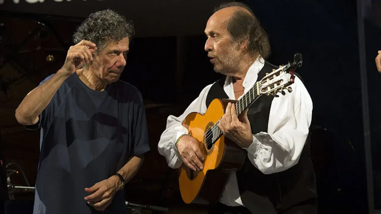 Chick Corea y Paco de Lucía, dos genios musicales, comparten un momento íntimo en el escenario, uno con el piano y el otro con su guitarra flamenca.