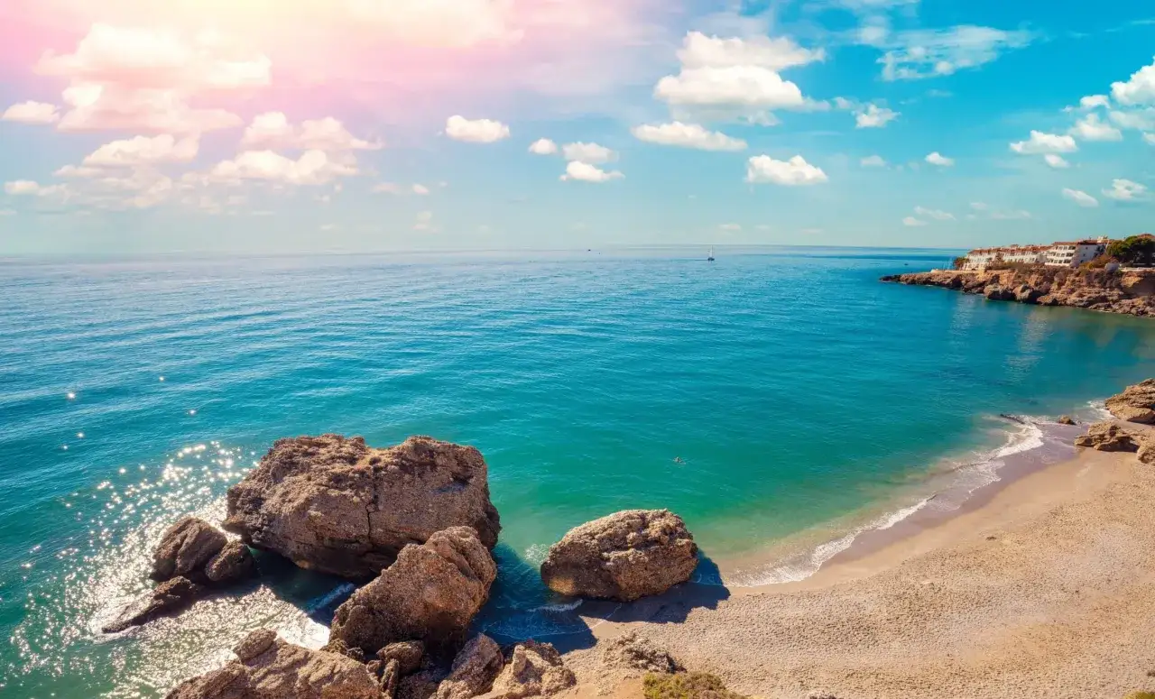Słoneczna plaża z klifami i białymi domkami, idealne miejsce na odkrywanie atrakcji Costa del Sol.