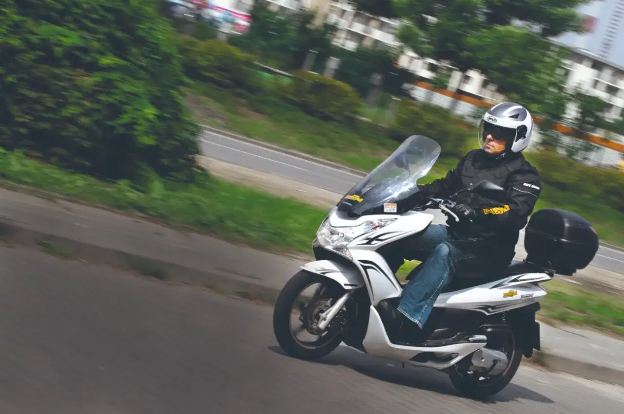 Mężczyzna w kasku jedzie białym skuterem Honda PCX 125. Dane techniczne tego modelu są imponujące.