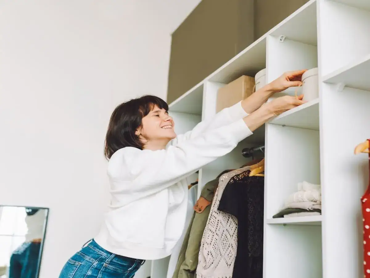 Frau r&auml;umt Kleiderschrank auf, der muffig riecht. Sie greift nach einer runden Box im obersten Fach.